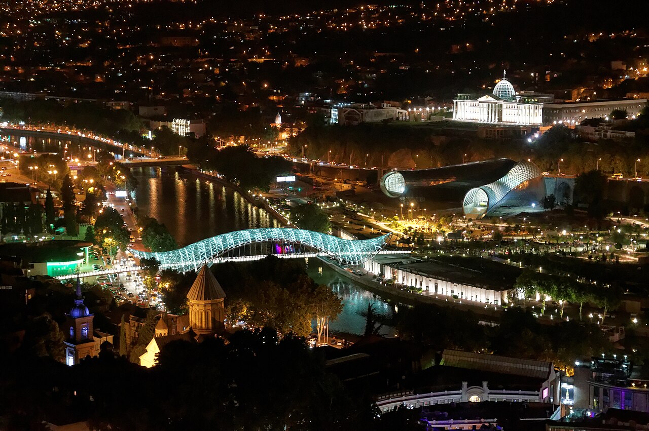 The Bridge of Peace illuminated at night over the Mtkvari River, with Sameba Cathedral in the background